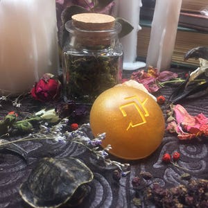 Puede incluir: Un orbe dorado con un s&iacute;mbolo dorado en &eacute;l, rodeado de flores secas y otros art&iacute;culos decorativos.