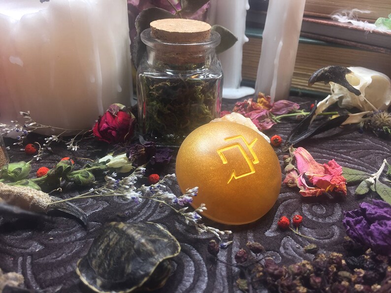 Puede incluir: Un orbe dorado con un s&iacute;mbolo dorado en &eacute;l, rodeado de flores secas y otros art&iacute;culos decorativos.