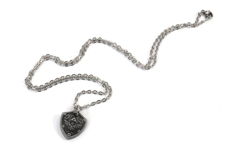 May include: A silver chain necklace with a pendant shaped like a shield with a design of a winged figure holding a sword.