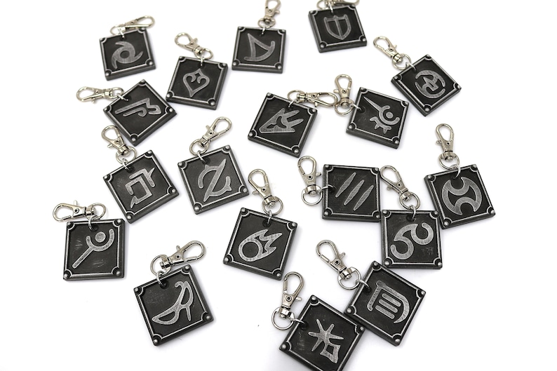May include: A set of 18 silver-colored metal keychains with different symbols on each. The keychains are square-shaped and have a silver-colored metal ring.