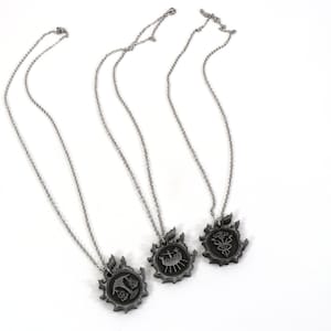 May include: Three silver necklaces with pendants featuring different designs. Each pendant is circular and has a detailed design within a larger circular frame.