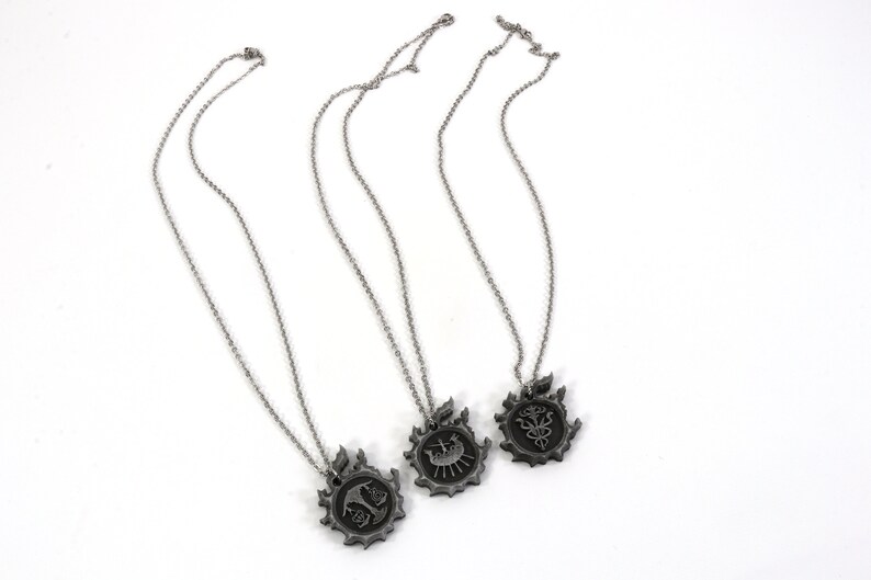 May include: Three silver necklaces with pendants featuring different designs. Each pendant is circular and has a detailed design within a larger circular frame.