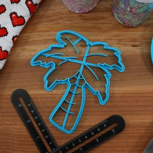 May include: A blue plastic palm tree cookie cutter on a wooden surface.