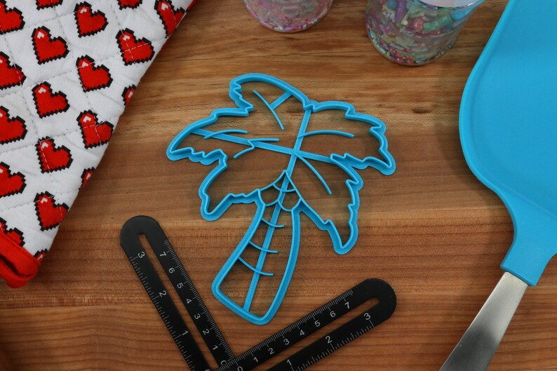 May include: A blue plastic palm tree cookie cutter on a wooden surface.