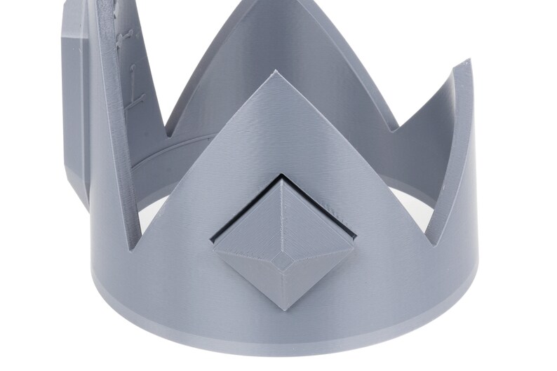 May include: A gray plastic crown with a diamond-shaped design in the center.