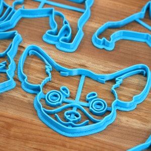 Puede incluir: Un juego de cortadores de galletas de pl&aacute;stico azul con forma de diferentes razas de perros. Los cortadores est&aacute;n sobre una superficie de madera.