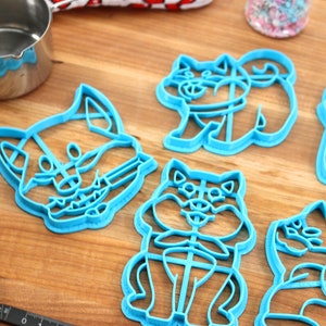 May include: Set of six blue plastic cookie cutters shaped like dogs. The cutters are on a wooden surface.