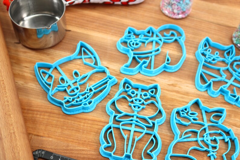 May include: Set of six blue plastic cookie cutters shaped like dogs. The cutters are on a wooden surface.