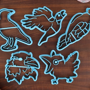 May include: Set of five blue plastic cookie cutters shaped like different birds. The cutters are on a brown wooden surface.