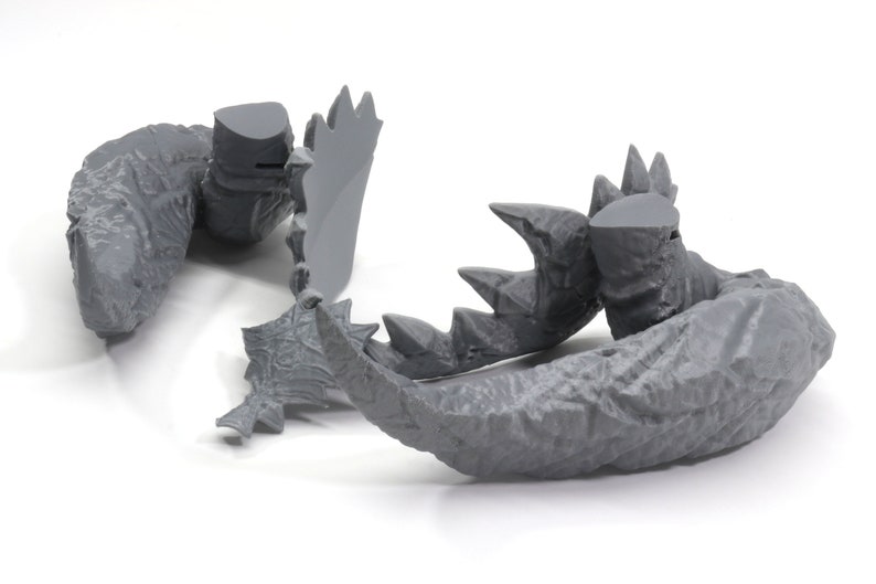 May include: Gray plastic model of a monster's tail with sharp claws and textured skin.