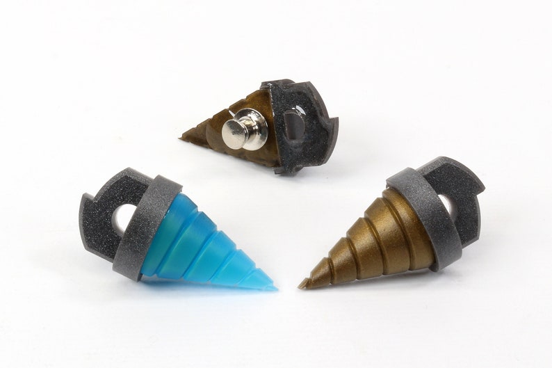 May include: Three drill-shaped pins with a unique design. One pin is blue, another is bronze, and the third is a combination of bronze and black. Each pin has a dark gray ring and a black backing with a pin clasp.