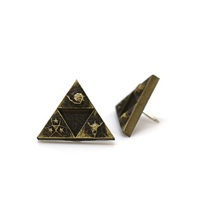 May include: A pair of gold-toned earrings featuring a triangular design with a stylized image of a triforce. The triforce is a symbol from the Legend of Zelda video game series.