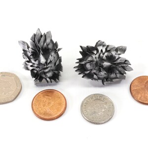 Pu&ograve; includere: Due sculture in metallo color argento di un viso con un motivo a foglie. Le sculture sono circa delle dimensioni di un centesimo americano.