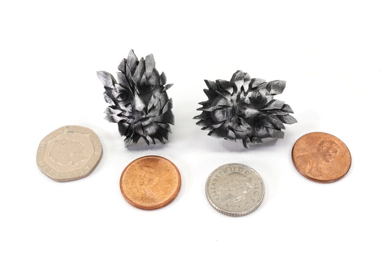 Pu&ograve; includere: Due sculture in metallo color argento di un viso con un motivo a foglie. Le sculture sono circa delle dimensioni di un centesimo americano.
