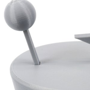 Pode incluir: Um modelo de sistema solar impresso em 3D cinza com um planeta e uma estrela. O planeta est&aacute; em um bast&atilde;o e a estrela est&aacute; em uma base.