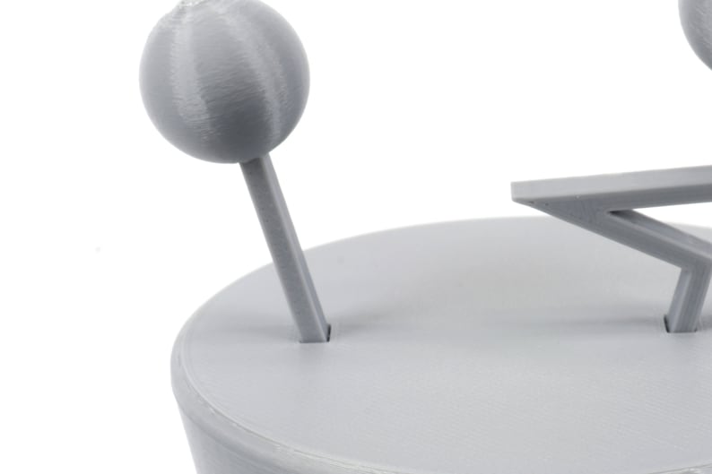 Pode incluir: Um modelo de sistema solar impresso em 3D cinza com um planeta e uma estrela. O planeta est&aacute; em um bast&atilde;o e a estrela est&aacute; em uma base.