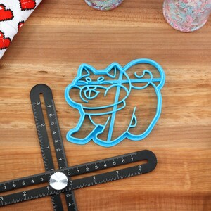 May include: A blue plastic cookie cutter shaped like a Shiba Inu dog. The cutter is on a wooden surface.