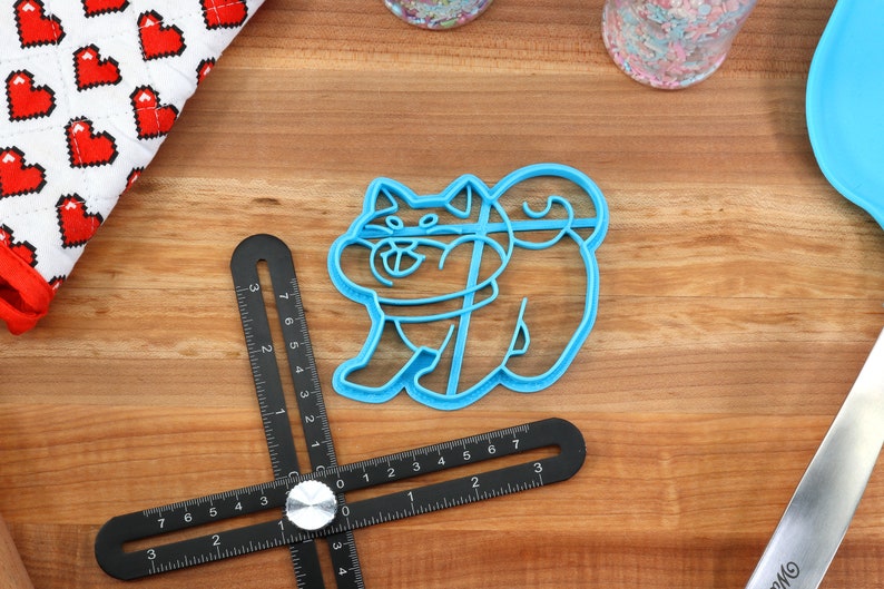 May include: A blue plastic cookie cutter shaped like a Shiba Inu dog. The cutter is on a wooden surface.
