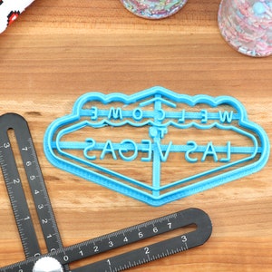 May include: Blue plastic cookie cutter shaped like the iconic "Welcome to Las Vegas" sign.