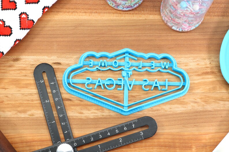 May include: Blue plastic cookie cutter shaped like the iconic "Welcome to Las Vegas" sign.