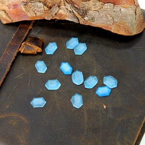 K&ouml;nnte beinhalten: Nahaufnahme eines braunen Lederjournals mit einem Riemen und einem Haufen hellblauer, facettierter Glassteine, die auf der Oberfl&auml;che verstreut sind.