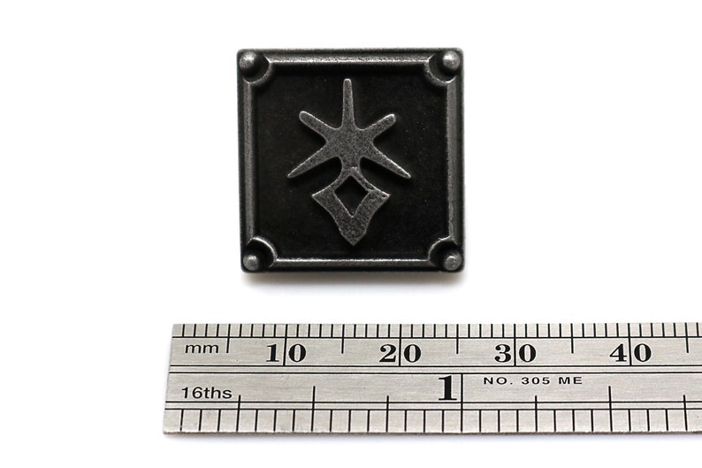 May include: A black metal pin with a stylized design of a star and a diamond shape. The pin is approximately 2 cm wide.