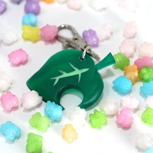 May include: A green leaf-shaped keychain with a white airplane design. The keychain is surrounded by colorful candy sprinkles.