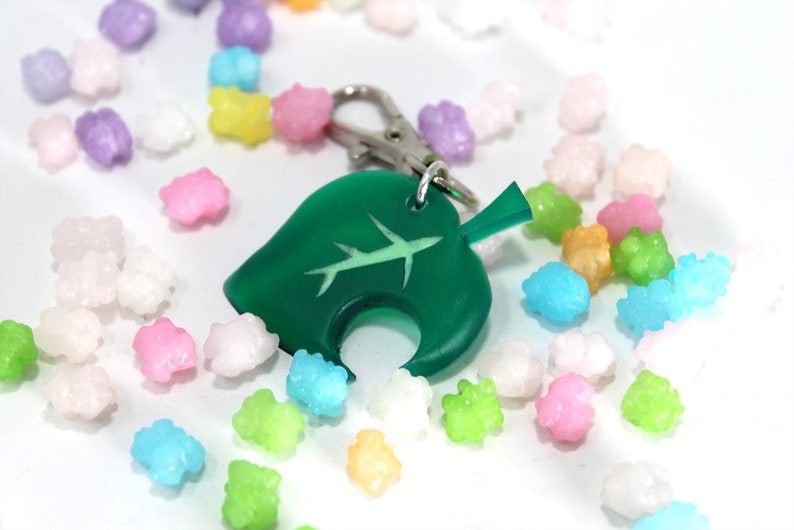 May include: A green leaf-shaped keychain with a white airplane design. The keychain is surrounded by colorful candy sprinkles.