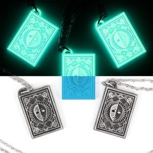 Puede incluir: Tres colgantes de plata con un dise&ntilde;o de cara en blanco y negro en una cadena. Los colgantes brillan en verde en la oscuridad.
