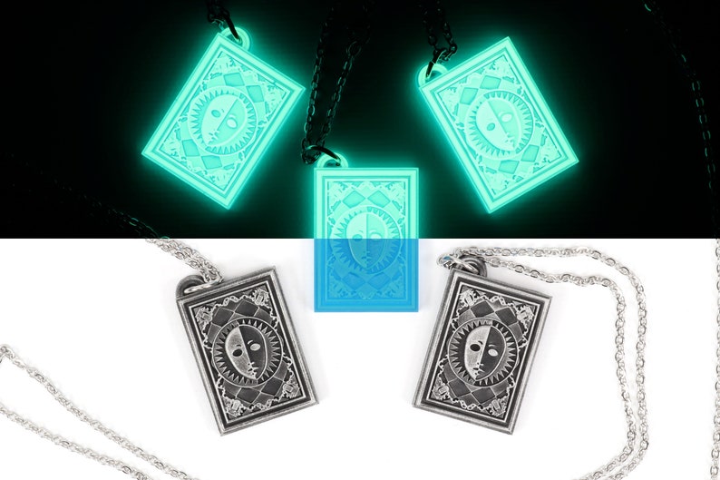Puede incluir: Tres colgantes de plata con un dise&ntilde;o de cara en blanco y negro en una cadena. Los colgantes brillan en verde en la oscuridad.