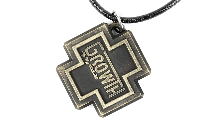 May include: A black metal pendant with a gold cross design and the word "GROWITH" inscribed on it. The pendant is attached to a black cord.