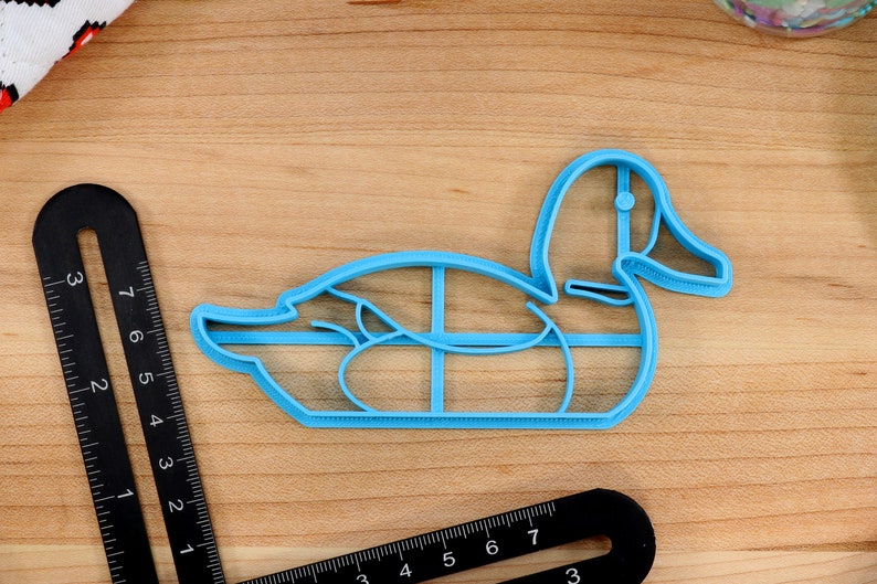 Op de afbeelding: Een lichtblauwe plastic eend koekjesvormer. De vormer is gevormd als een eend met een lange snavel en een rond lichaam.