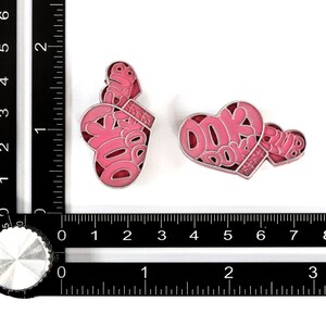 May include: Two pink enamel pins in the shape of hearts. One heart has the text "DOK DOK CLUB" inside. The other heart has the text "CLUB" inside.
