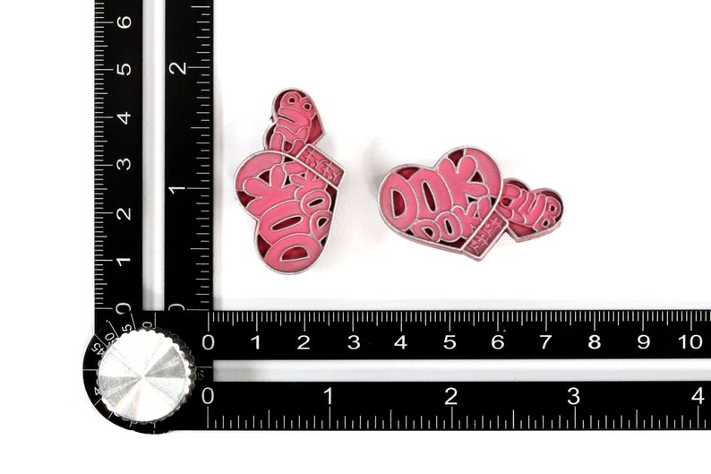 May include: Two pink enamel pins in the shape of hearts. One heart has the text "DOK DOK CLUB" inside. The other heart has the text "CLUB" inside.