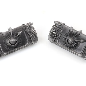May include: Two silver-coloured metal keychains with intricate designs. Each keychain features a circular centre with a raised arrow and a detailed, textured border.