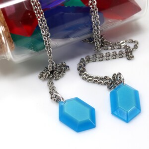 May include: Two silver chains with blue gemstone pendants hanging from a glass bottle filled with colorful confetti.