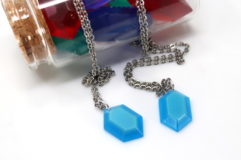 May include: Two silver chains with blue gemstone pendants hanging from a glass bottle filled with colorful confetti.