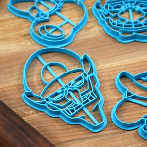 May include: A set of six blue plastic cookie cutters shaped like cartoon characters. The cutters are on a wooden surface.