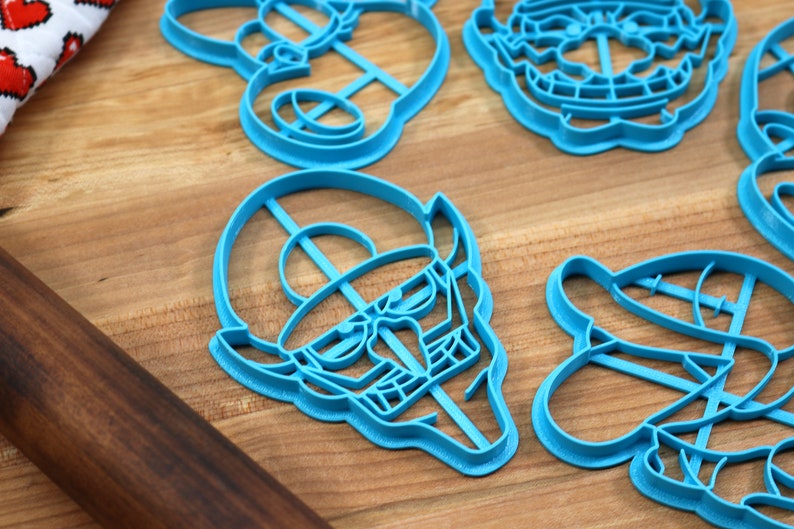 May include: A set of six blue plastic cookie cutters shaped like cartoon characters. The cutters are on a wooden surface.