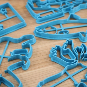 May include: A set of blue plastic cookie cutters in various shapes, including a fish, a reindeer, a star, and a geometric design.