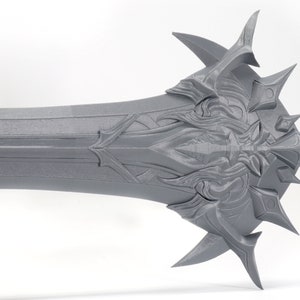 Puede incluir: Una espada gris impresa en 3D con una empu&ntilde;adura detallada y adornada y una punta afilada.