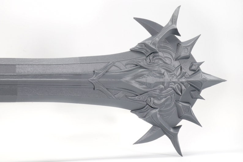 Puede incluir: Una espada gris impresa en 3D con una empu&ntilde;adura detallada y adornada y una punta afilada.