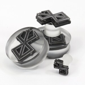 May include: Three clear acrylic ear gauges with a black geometric design. The gauges are in different sizes and are stacked on top of each other.