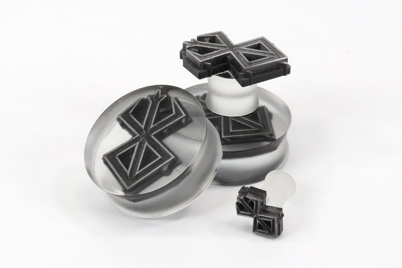 May include: Three clear acrylic ear gauges with a black geometric design. The gauges are in different sizes and are stacked on top of each other.