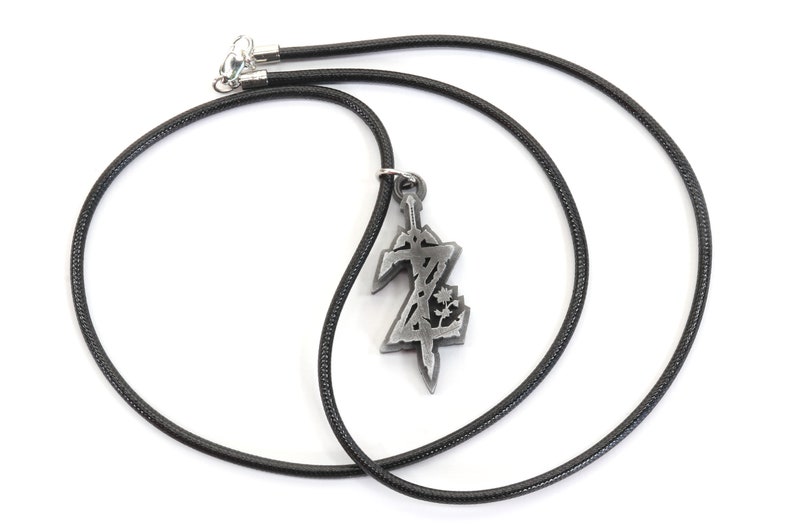 May include: A black cord necklace with a silver pendant featuring a stylized sword and the letter Z.
