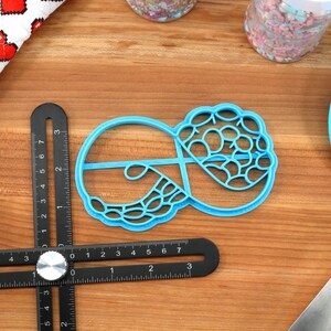 May include: A blue plastic cookie cutter shaped like a donut with a decorative design. The cutter is on a wooden surface.