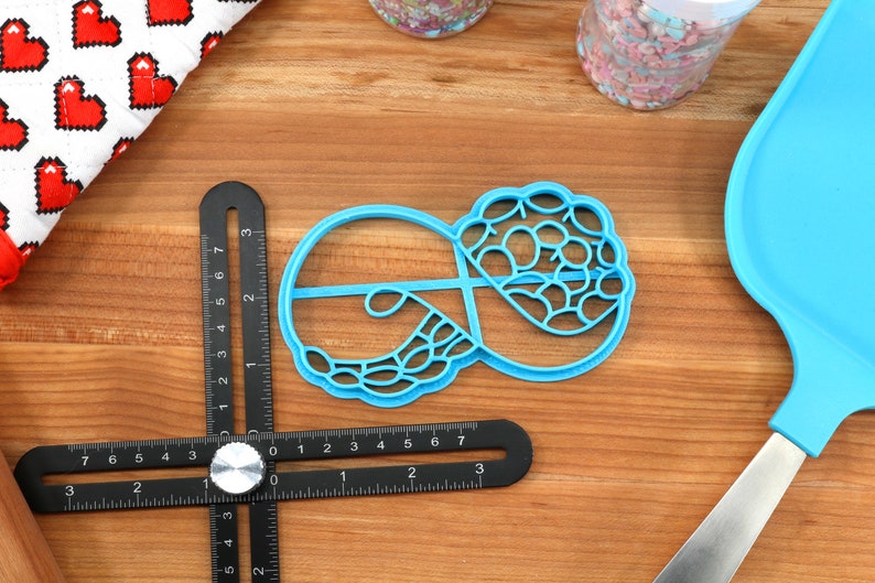 May include: A blue plastic cookie cutter shaped like a donut with a decorative design. The cutter is on a wooden surface.