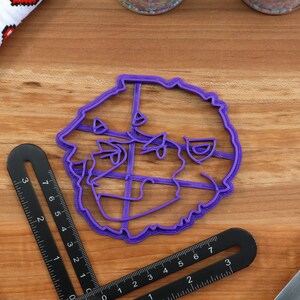 May include: Purple plastic cookie cutter shaped like a dog's head. The cutter has a detailed design with a fluffy texture.