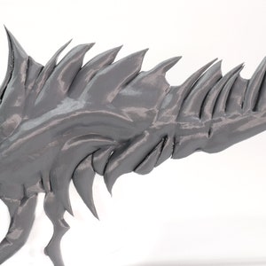 May include: A gray 3D printed model of a dragon's wing with sharp, jagged edges.