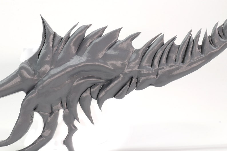 May include: A gray 3D printed model of a dragon's wing with sharp, jagged edges.